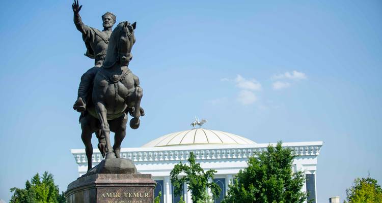 Statue équestre d'Amir Temur sur un haut socle avec un bâtiment blanc à dôme en arrière-plan