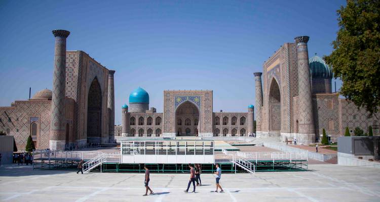 Vaste place du Registan avec trois grandes façades de madrasas et des visiteurs traversant la plaza