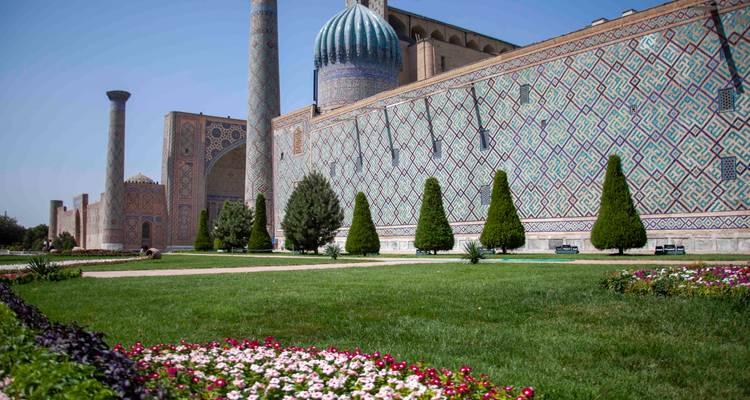 Mur latéral d'une madrasa richement carrelée bordant une pelouse soignée avec des parterres de fleurs colorées