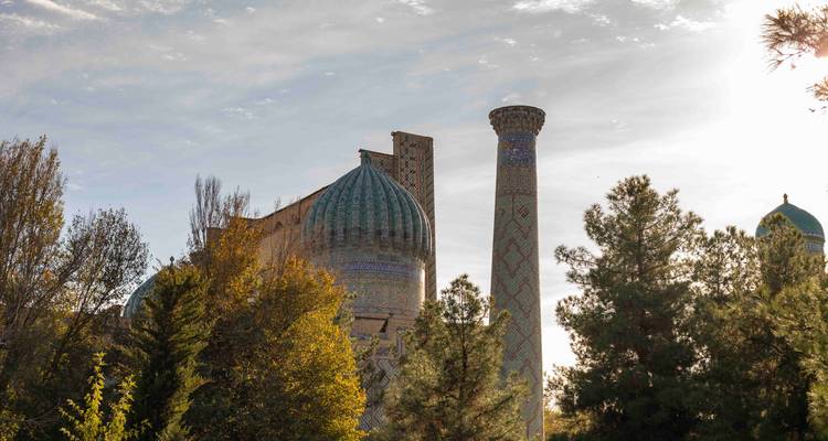 Mausolée au dôme turquoise s'élevant au-delà des arbres d'automne avec le soleil bas dans le ciel