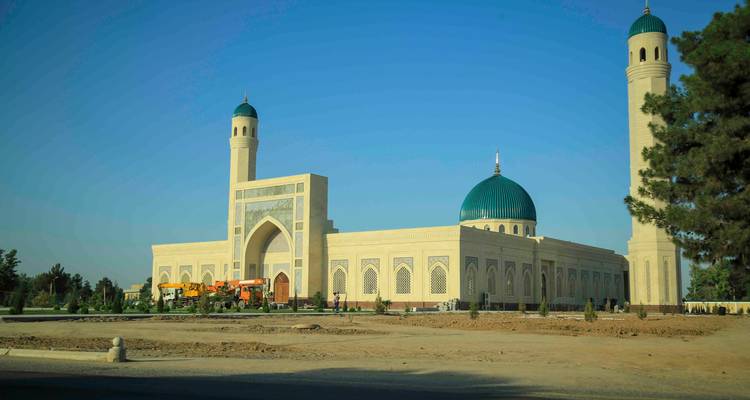 Grande mosquée moderne avec un dôme émeraude et deux minarets beiges s'élevant contre un ciel matinal bleu profond.