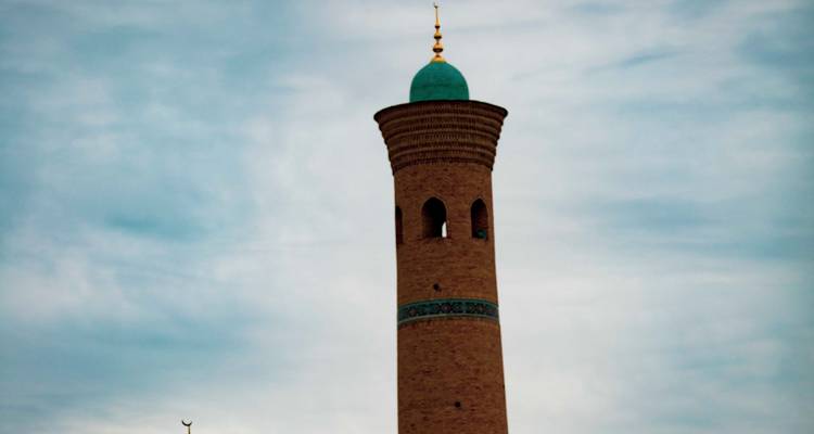 Minaret en brique unique surmonté d'un dôme turquoise se dressant contre un ciel nuageux.