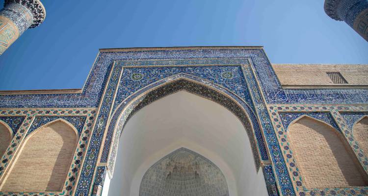 Portail voûté aux carreaux bleus d'une madrassa islamique photographié en contre-plongée sur un ciel dégagé.