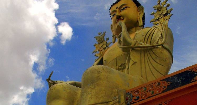 Große goldene sitzende Buddha-Statue vor einem teilweise bewölkten Himmel.