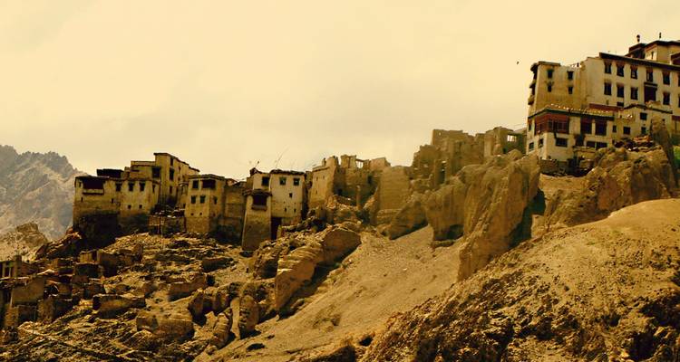Weather-worn cliffside village ruins under a hazy golden light.
