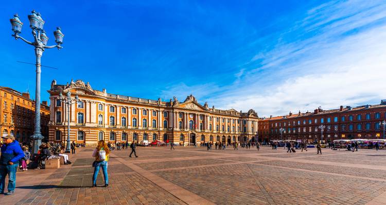 Lebendiger Capitole-Platz in Toulouse mit großartiger neoklassizistischer Fassade und Einheimischen, die über den sonnenbeschienenen Platz spazieren.
