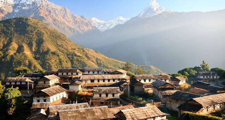 Terrassenförmiges Bergdorf aus Steinhäusern, das in warmem Licht unter schneebedeckten Himalaya-Gipfeln ruht