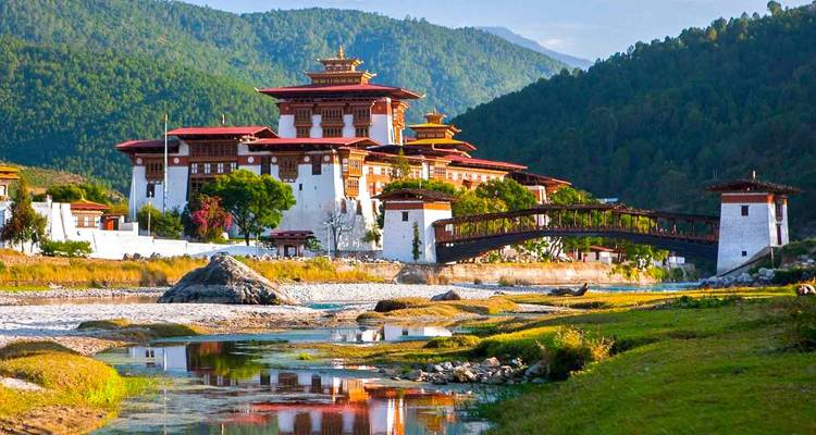 Majestätische Punakha Dzong mit lebendigen roten und weißen Ebenen neben einem reflektierenden Fluss und bewaldeten Hügeln