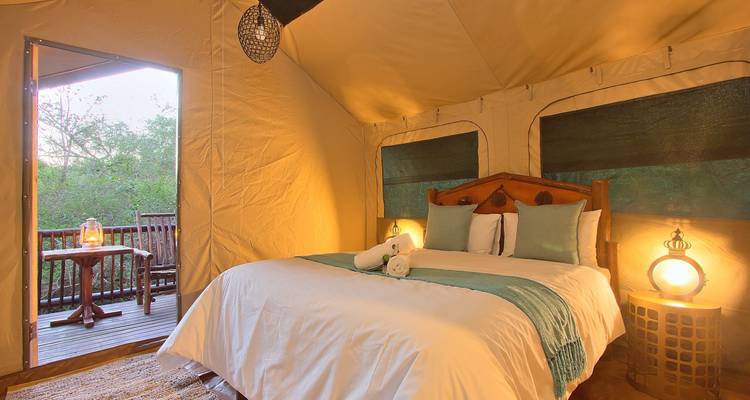 Gemütliches Interieur eines Safari-Zeltes mit Doppelbett, zusammengerollten Handtüchern und warmer Laternenbeleuchtung.