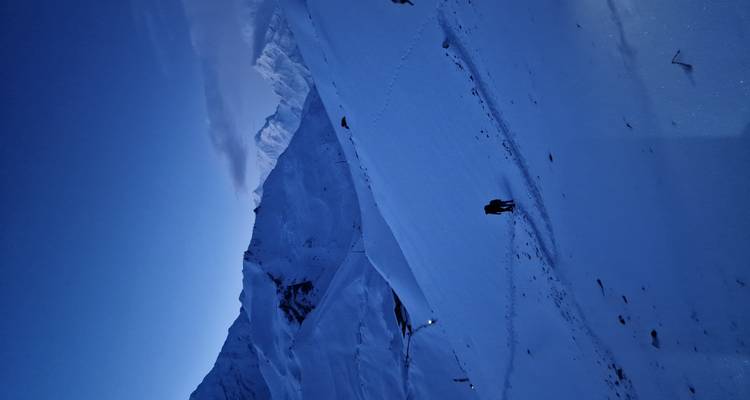 Lone trekker walks across silent, moonlit snowfields surrounded by high Himalayan peaks.