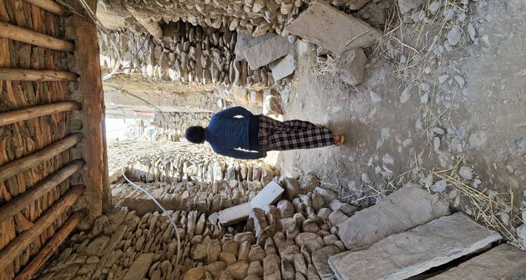 Person in traditional clothes walks through narrow stone alley with wooden beams overhead.