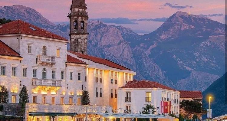 Elegante waterfront stad Perast met klokkentoren omlijst door ruige bergen in de gloed van de zonsondergang.