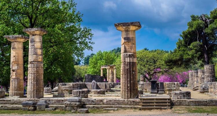 Stone column remains and flowering trees at the archaeological site of Olympia