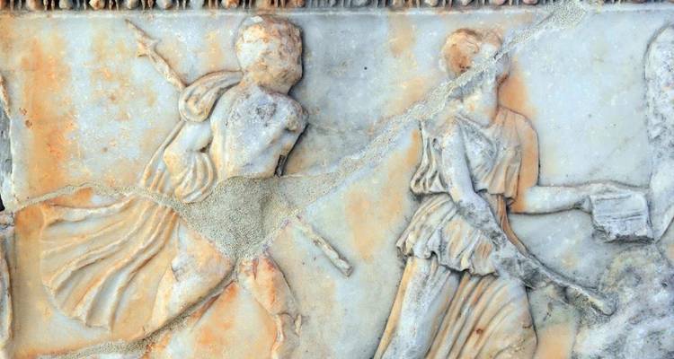 Close-up of weathered classical marble relief depicting human figures in motion.