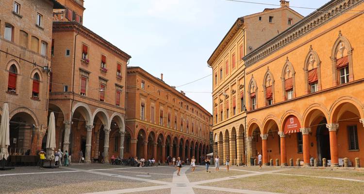Plaza medieval bordeada de pórticos en Bolonia con lugareños y visitantes paseando bajo las arcadas
