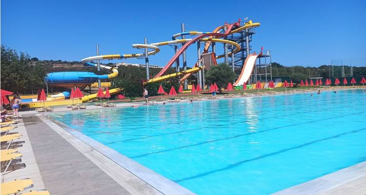 Outdoor-Wasserpark mit gewundenen gelben und roten Rutschen neben einem großen blauen Schwimmbecken und Sonnenliegen.