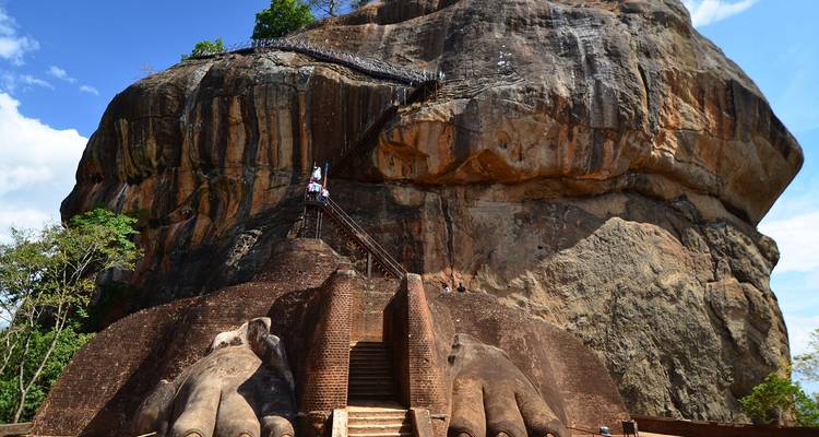 Turistas subiendo la escalera en la Roca de Sigiriya enmarcados por el cielo azul y los acantilados de color naranja-marrón.