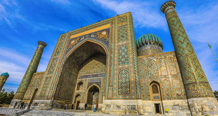 Grand mosaic-covered portal and turquoise dome of the Registan’s Sher-Dor Madrasa against a vivid blue sky.