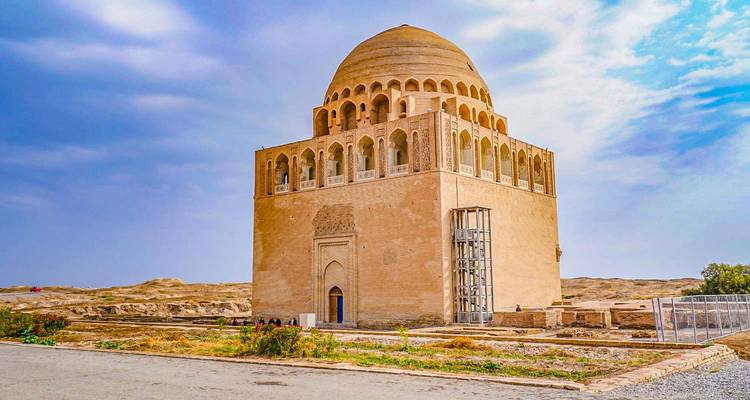 Isolated brick mausoleum with arched windows and domed roof standing in a dry desert archaeological site.