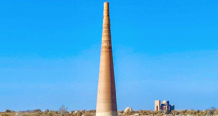Tall, slender brick minaret rising against a cloudless azure sky on a flat desert plain.