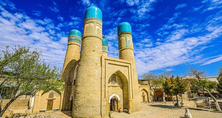 Chor Minor’s four turquoise-topped towers stand beneath a speckled blue sky, visitors entering the arched doorway.
