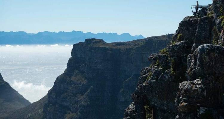 Dramatic cliff edge of Table Mountain with cloud inversions and distant mountain ridges.