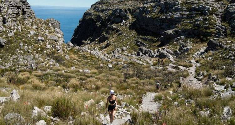 Los excursionistas ascienden por un valle escarpado en Table Mountain rodeados de fynbos y el mar distante.