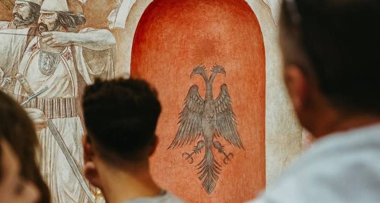 Tourists observe a fresco featuring Albania’s double-headed eagle emblem inside a historic building.