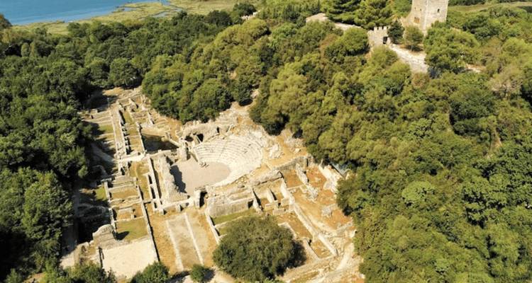 Vista aérea de anfiteatro antiguo y ruinas rodeadas por bosque denso en el sitio arqueológico de Butrinto.