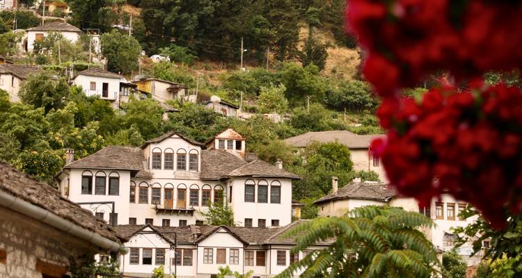 Historic Ottoman-era houses nestled on a green hillside framed by red bougainvillea