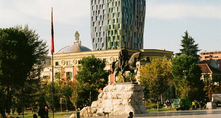 Equestrian statue of Skanderbeg in Tirana’s main square framed by modern skyscraper and historic buildings.