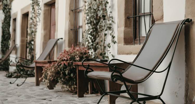 Quiet stone courtyard with wrought-iron loungers and potted plants along a rustic wall.