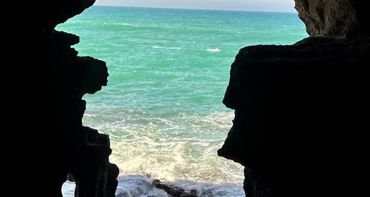 View of turquoise waves through the dark opening of a seaside cave.