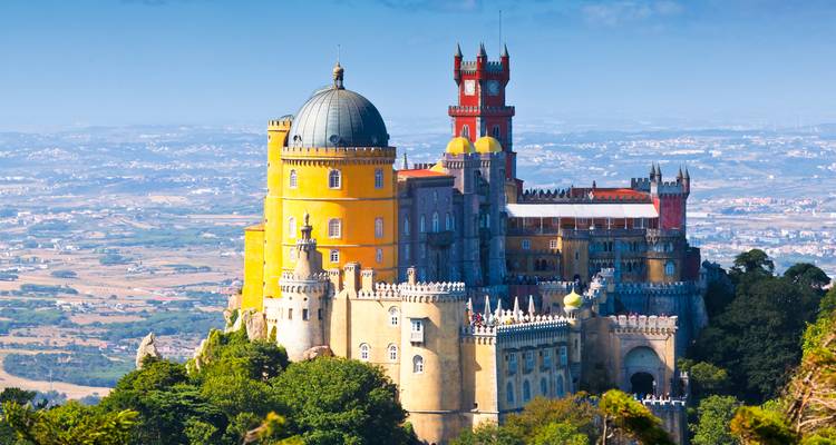 Fairy-tale Pena Palace with its vivid yellow and red towers perched atop green Sintra hills under blue sky.