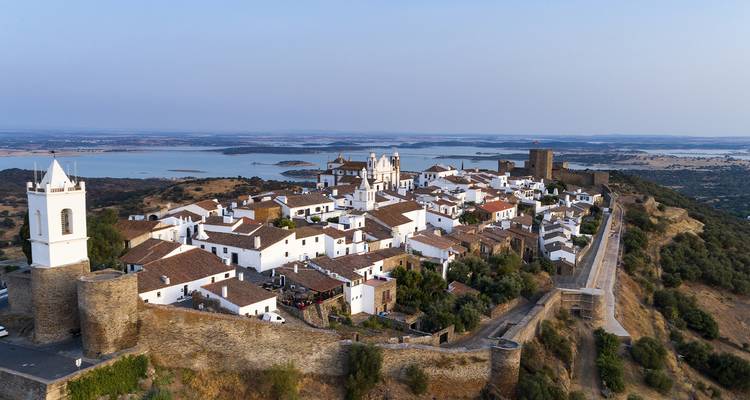 Village blanchi à la chaux de Monsaraz au sommet d'une colline avec les plaines environnantes et vues sur le lac lointain à la lumière du coucher du soleil.