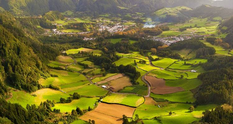 Patchwork of lush green fields and forests in a volcanic valley with distant village