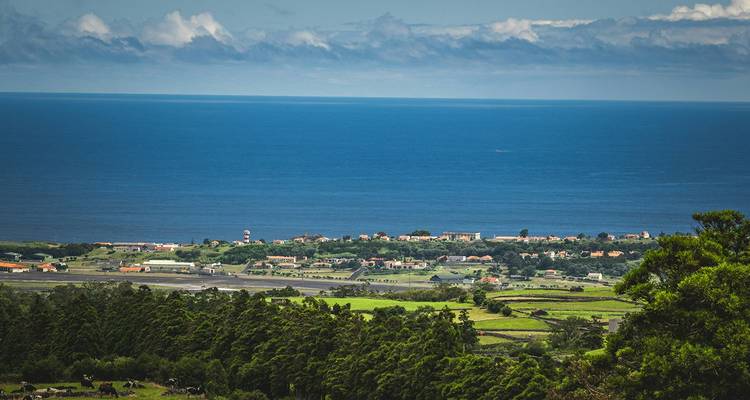 Wide ocean view with green patchwork fields and village on distant shoreline