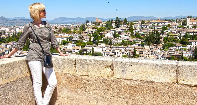 Vrouw geniet van een panoramisch uitzicht over Granada's witte huizen en met cipressen bezaaide heuvels vanaf oude stadsmuren.