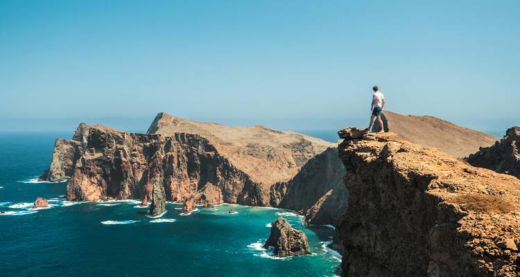 Eenzame wandelaar staand op dramatische kliffrand met uitzicht op ruige kustlijn van Madeira en turquoise zee