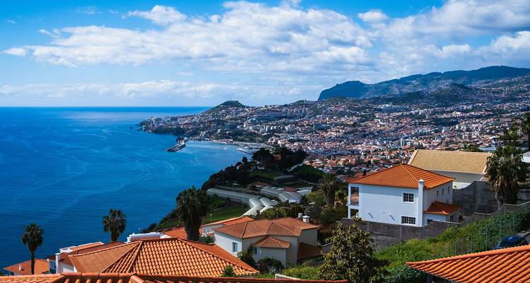 Panoramic view over Funchal’s terracotta rooftops, harbour and surrounding mountains on a sunny day.