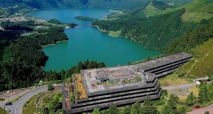 Aerial view of twin-colored Sete Cidades volcanic lakes bordered by lush green cliffs, abandoned lakeside hotel in foreground.