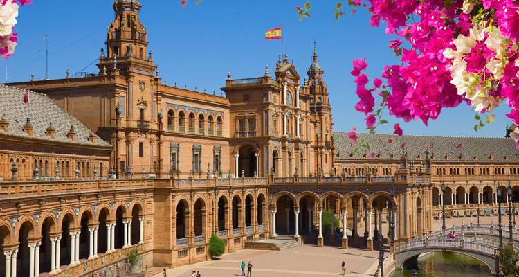 Der großartige halbkreisförmige Plaza de España in Sevilla, umrahmt von leuchtend rosa Bougainvillea-Blüten unter einem klaren Himmel.