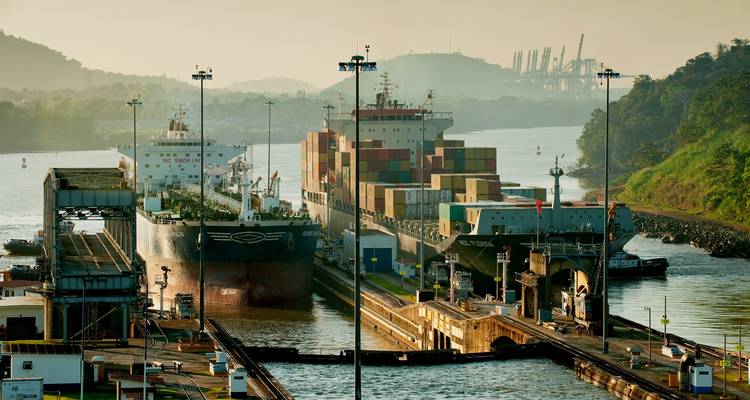 Containerschiffe durchfahren ein Schleusensystem des Panamakanals mit nebligen grünen Hügeln im Hintergrund bei warmem Licht