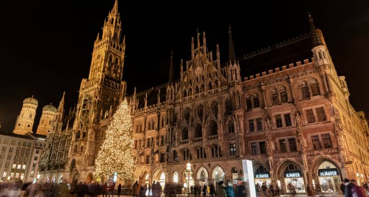 Night view of Munich’s ornate town hall and glittering Christmas tree lighting up Marienplatz filled with blurred passers-by.