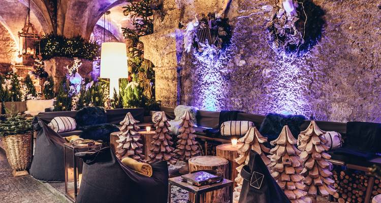 Atmospheric vaulted lounge with plush seating and wood-carved decorations bathed in moody purple lighting.