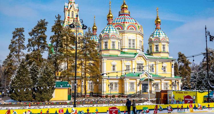 La Catedral de Zenkov de un amarillo brillante con cúpulas coloridas se alza en un parque nevado decorado con luces festivas y banderas.