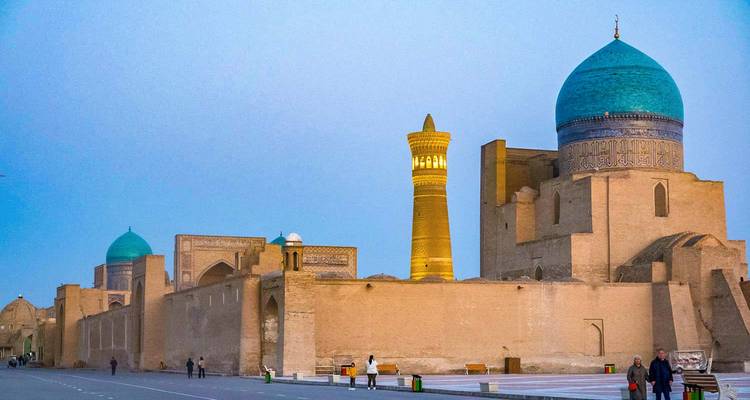 Escena nocturna de los antiguos muros de la ciudad de Bujará con el Minarete de Kalón iluminado contra un cielo pálido.