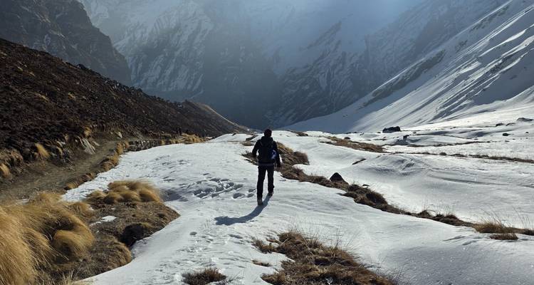 A hiker makes their way through windswept snow in a dramatic Himalayan gorge.