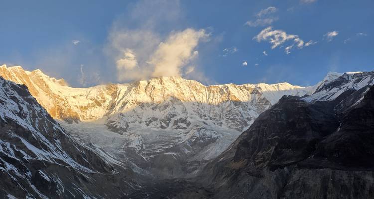 Sunset light bathes the towering snow-capped walls of the Annapurna massif with wisps of cloud rising.