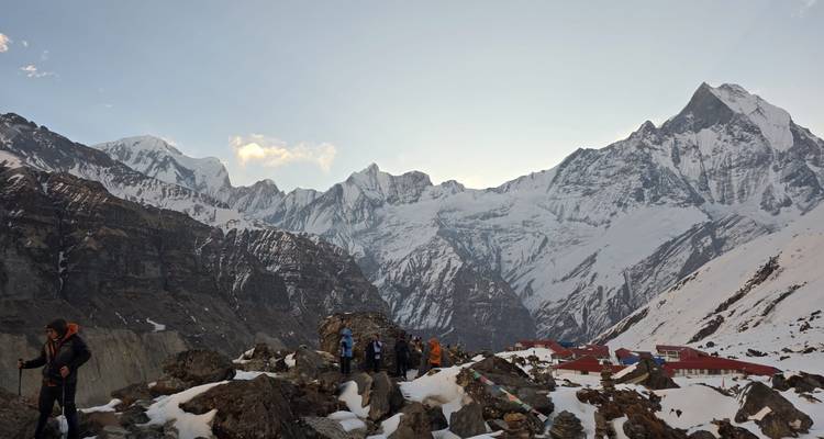 Trekkers gather on a rocky outcrop above Annapurna Base Camp with evening light on serrated peaks.